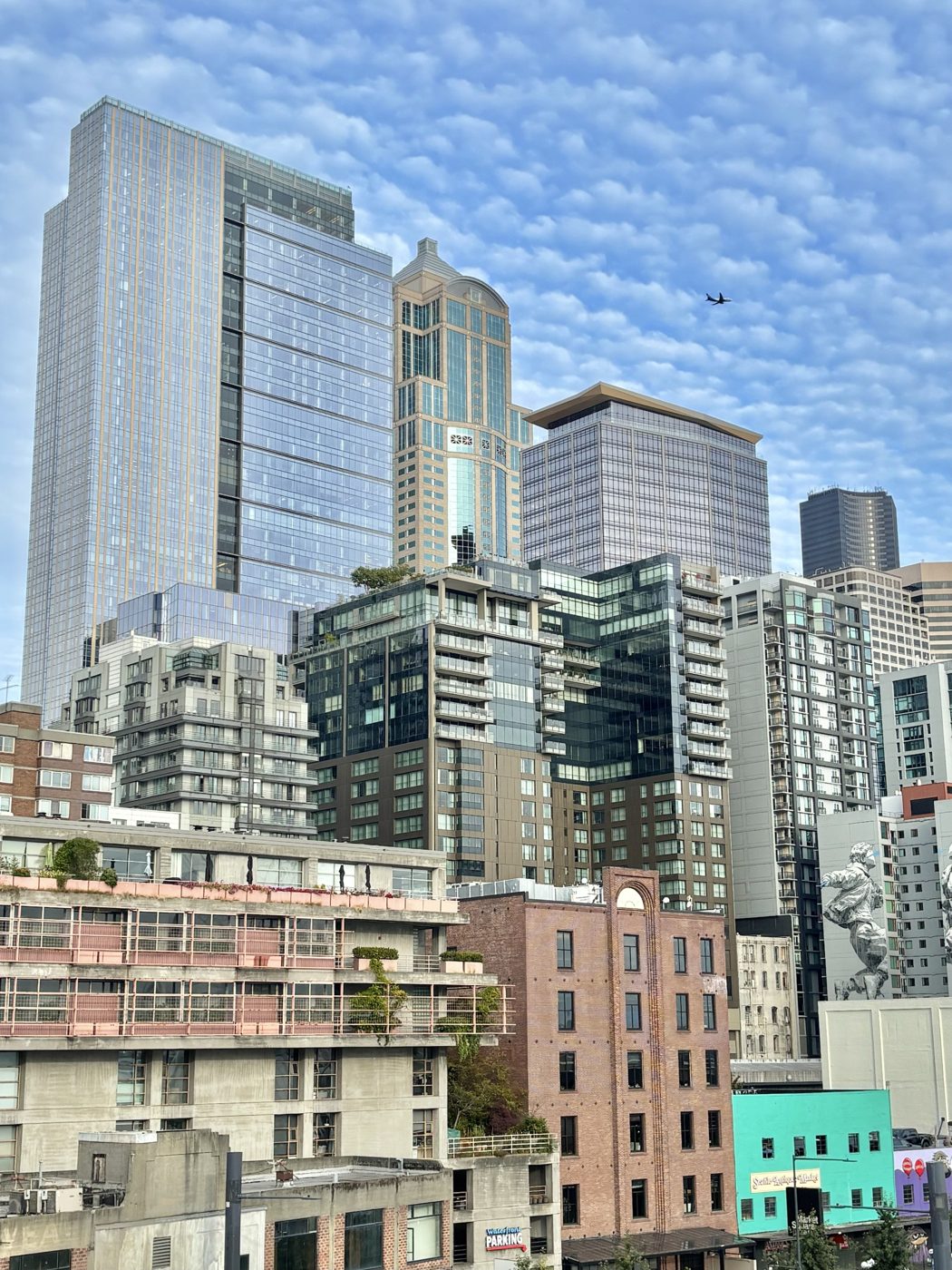 Downtown Seattle towers under a sky of small clouds, with a plane passing overhead